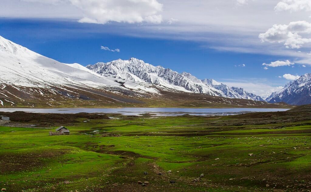 Snowy mountains above green meadows and Shandur Lake in Pakistan